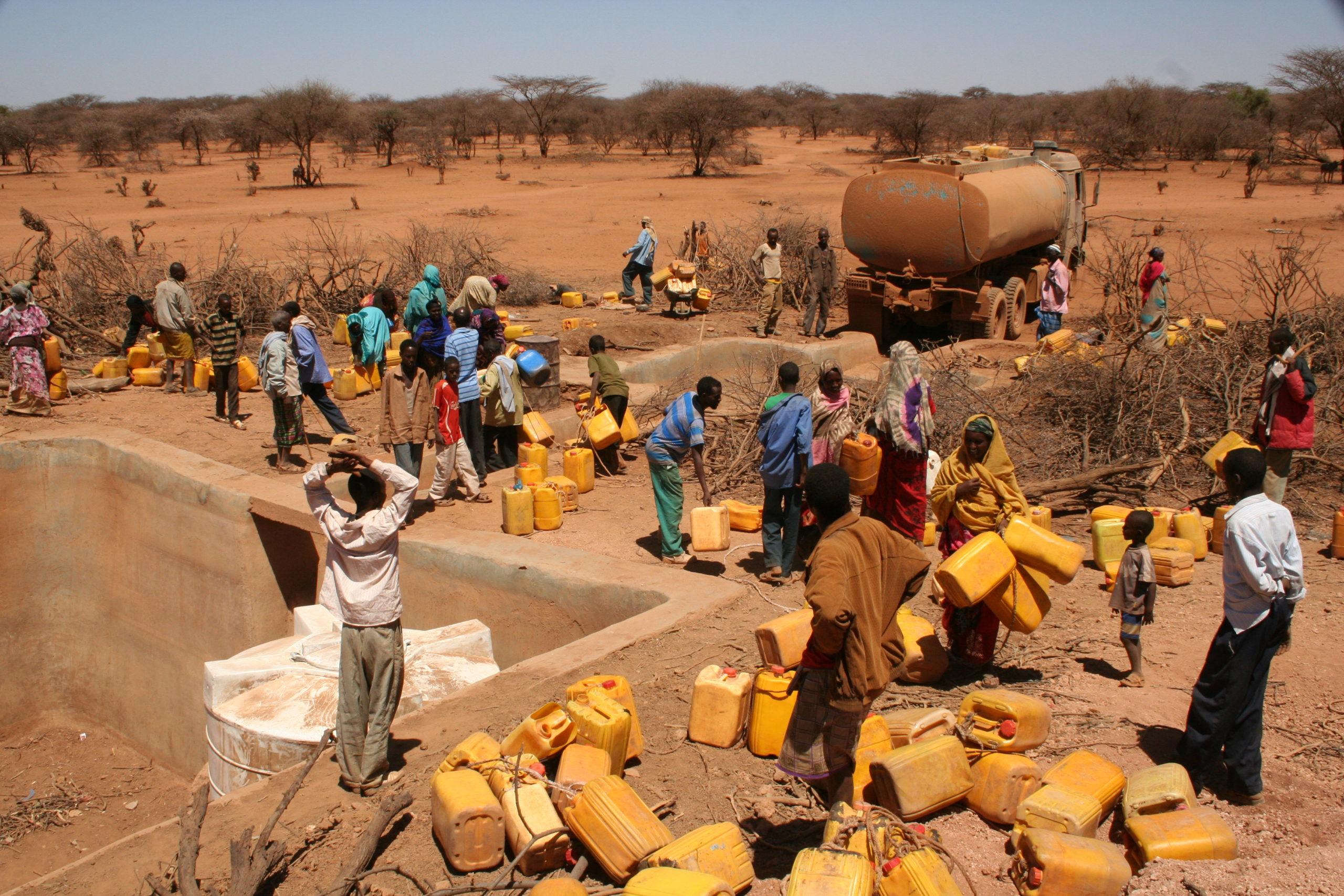 A dried up water distribution with many people with jerrycans waiting for water
